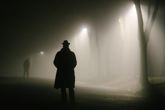Silhouette of a mysterious man walking under streetlights at night.